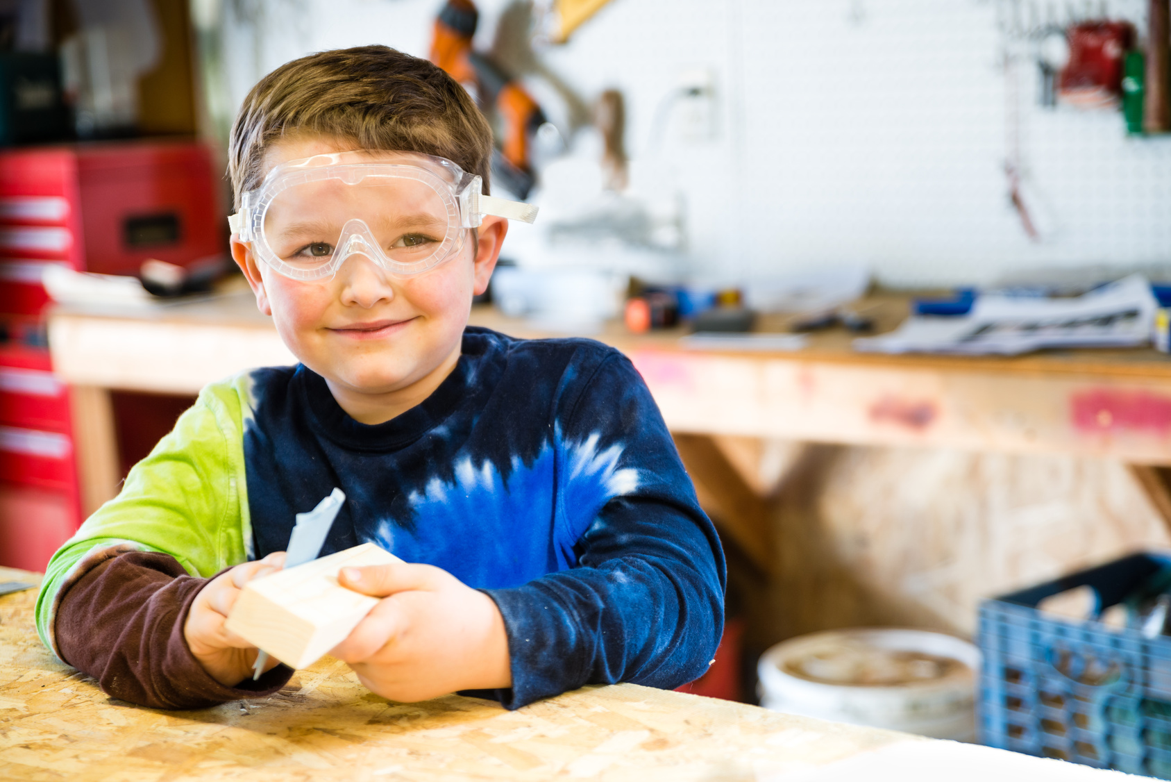 Boy sanding wooden block in workshop as he builds car for Pinewood Derby