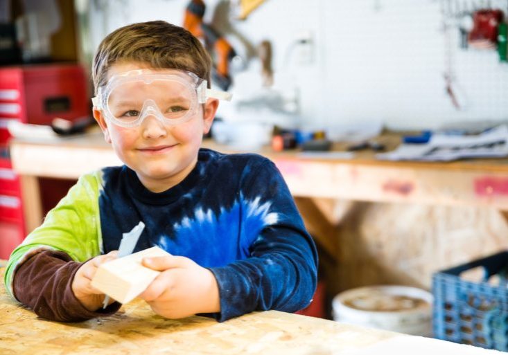 Boy sanding wooden block in workshop as he builds car for Pinewood Derby